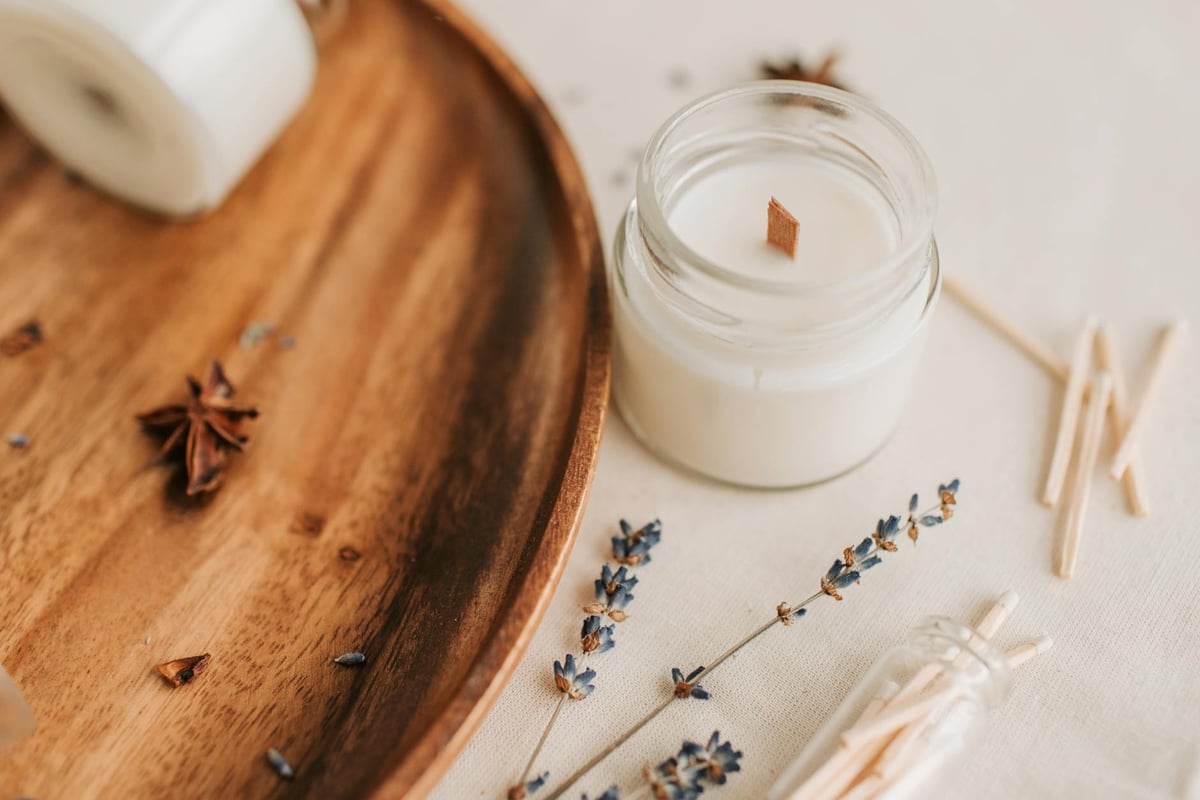 Close-up of a lavender-scented candle in a jar with decor on a wooden tray.