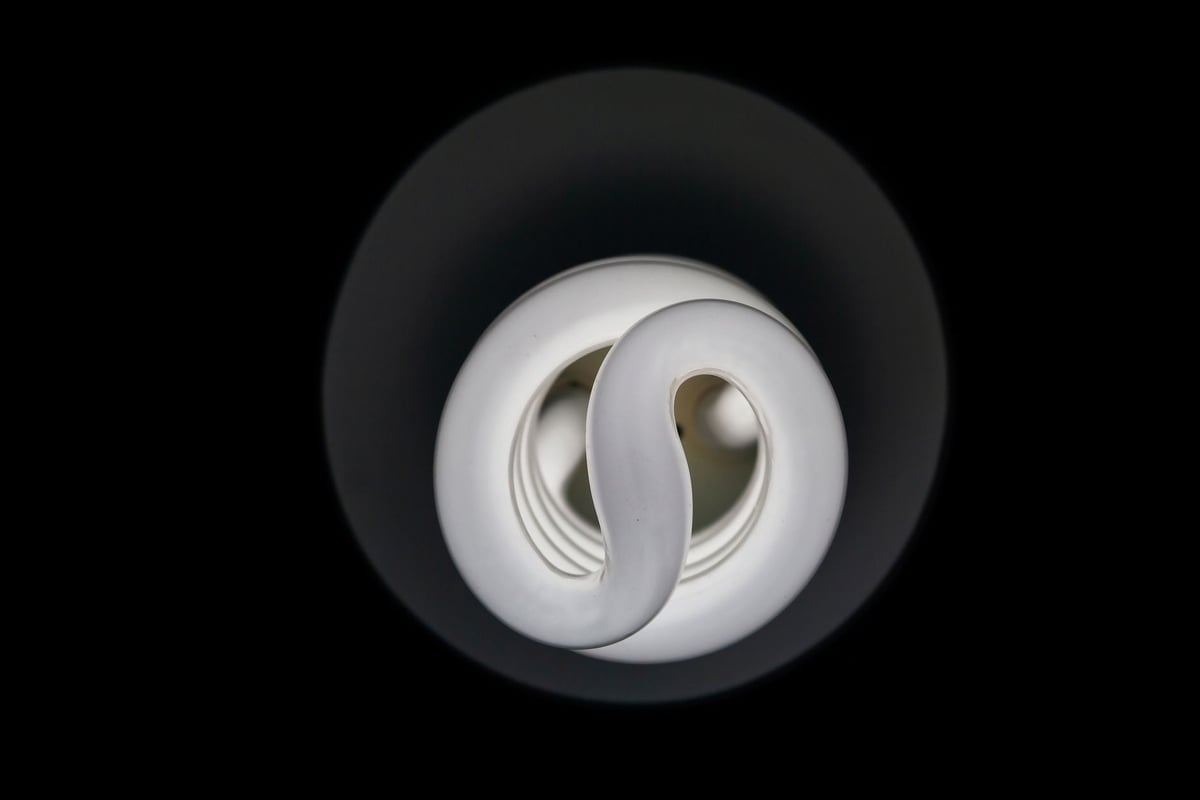 A detailed view of a compact fluorescent lamp (CFL) bulb against a dark background, highlighting its spiral design.