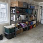 Metal storage shelves with paint cans, bins and a bag of pet food in an attached garage in winter.