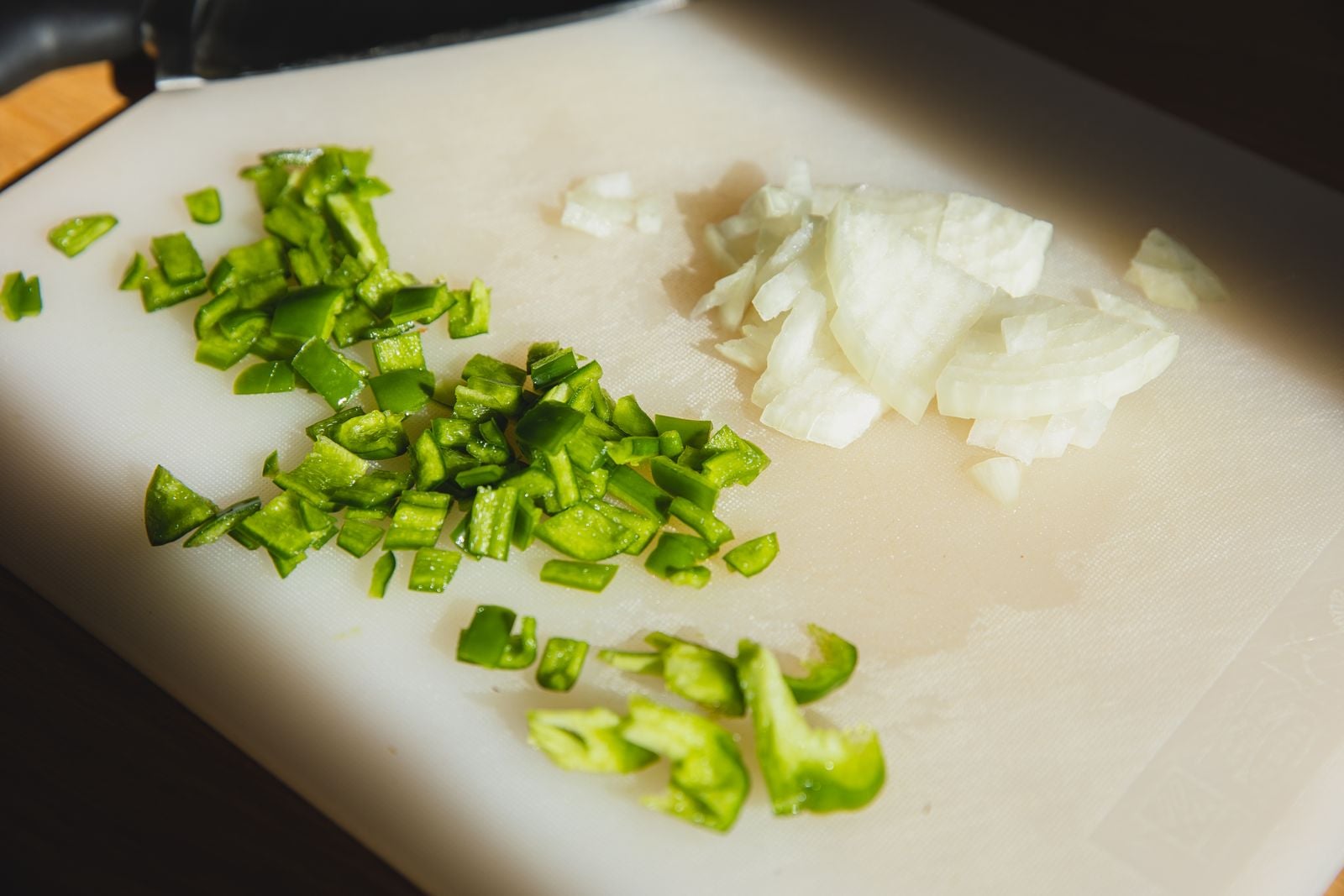 Chopped green pepper and onion on a white plastic cutting board.