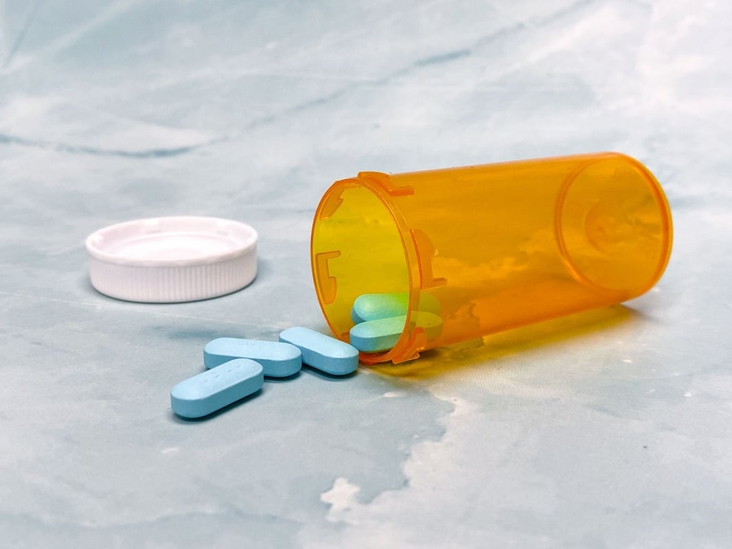 Close-up of blue tablets spilling from an orange prescription bottle on a marble surface.