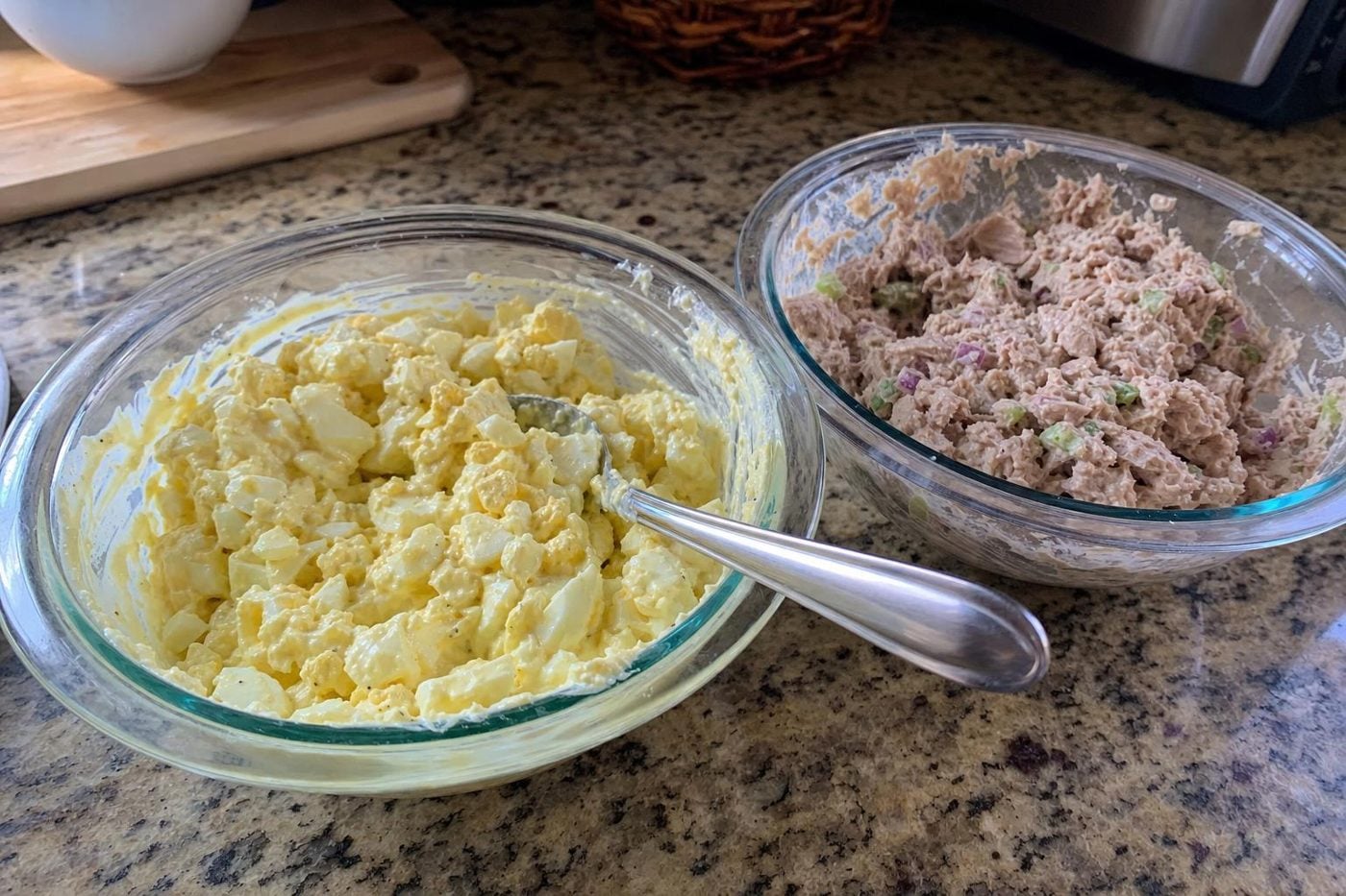 Bowls of egg salad and tuna salad made with mayonnaise on a kitchen counter.
