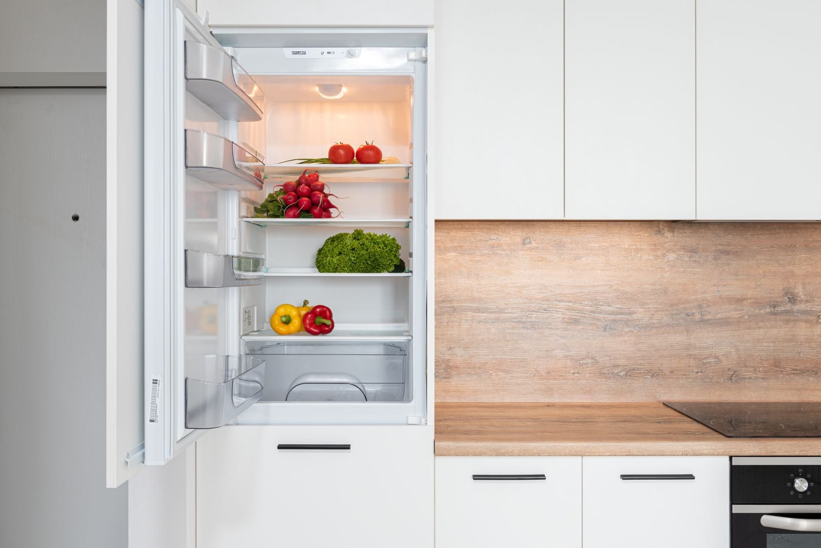 An open refrigerator with fresh vegetables on the shelves in a home kitchen.