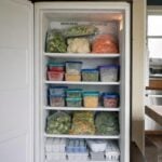 An open upright home freezer filled with bagged frozen vegetables and labeled containers.