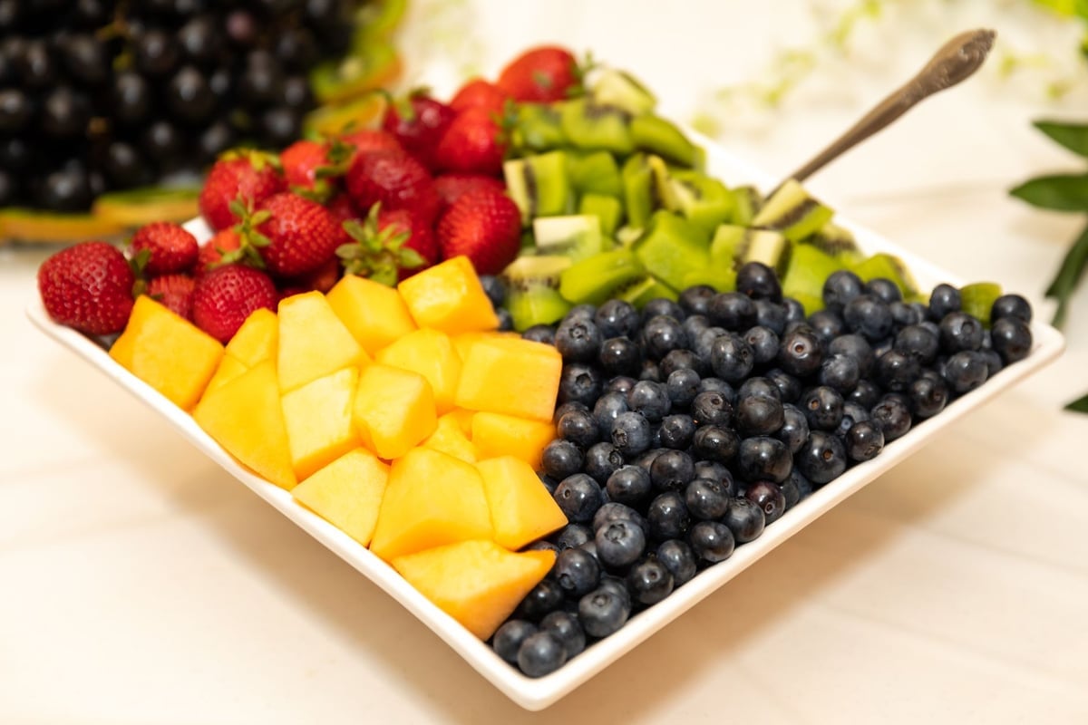 Vibrant platter of fresh cut fruit including strawberries, blueberries, kiwi, and melons.