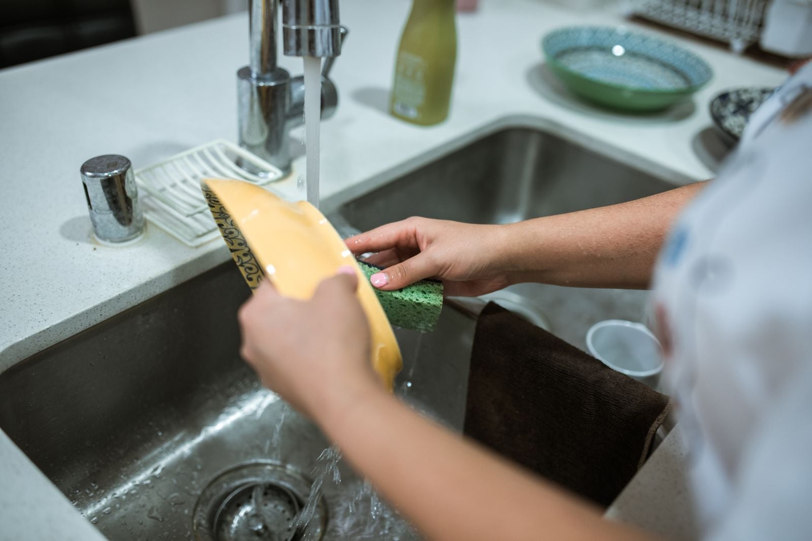 Hands washing a dish with a sponge at a kitchen sink.